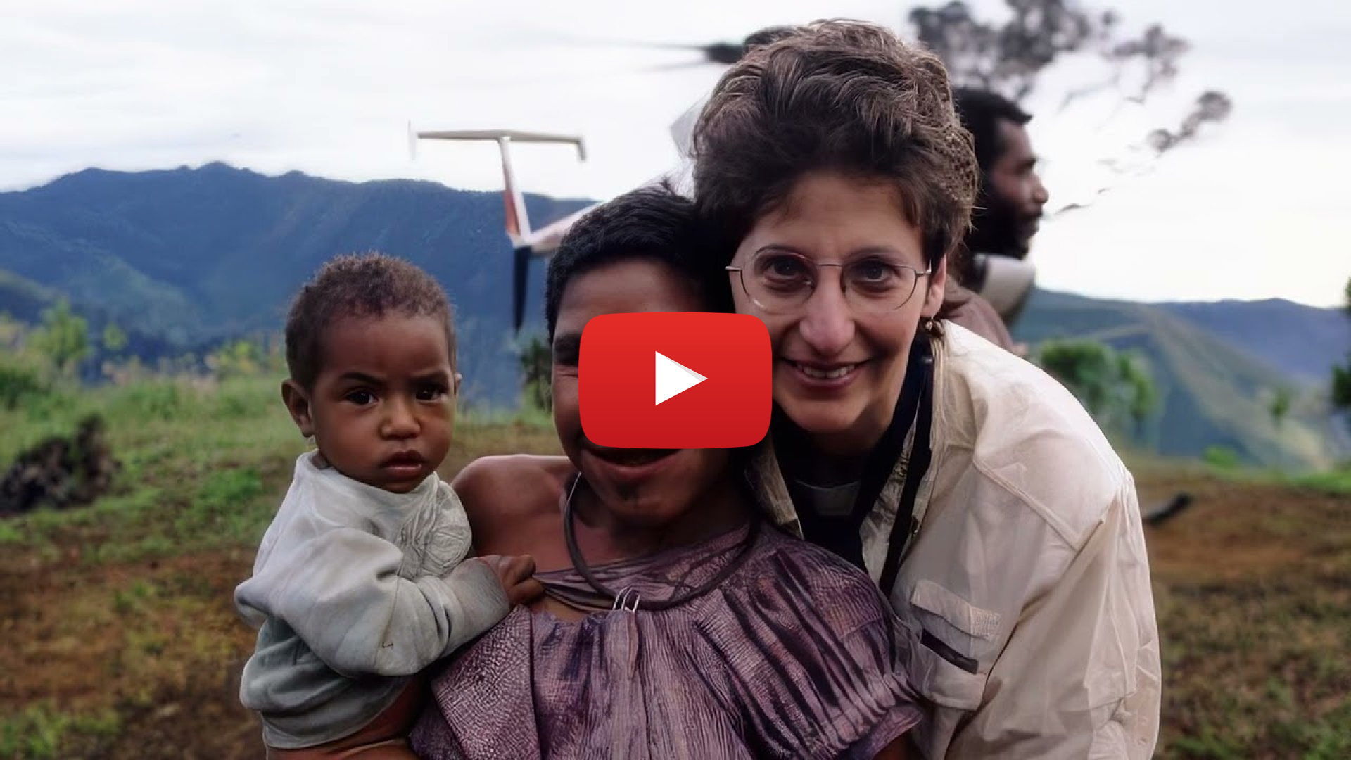 A closeup of two women, one of them holding a small child, posing in front of a helicopter.