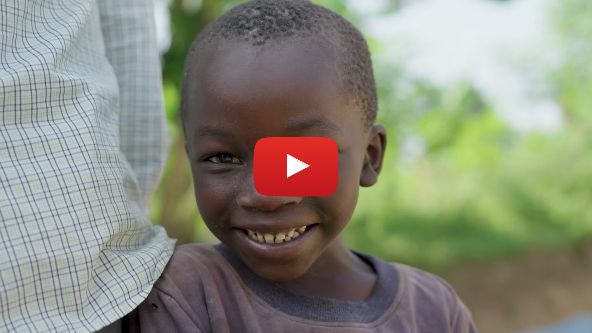 A closeup of a young boy smiling. Overlaid is a video play button.