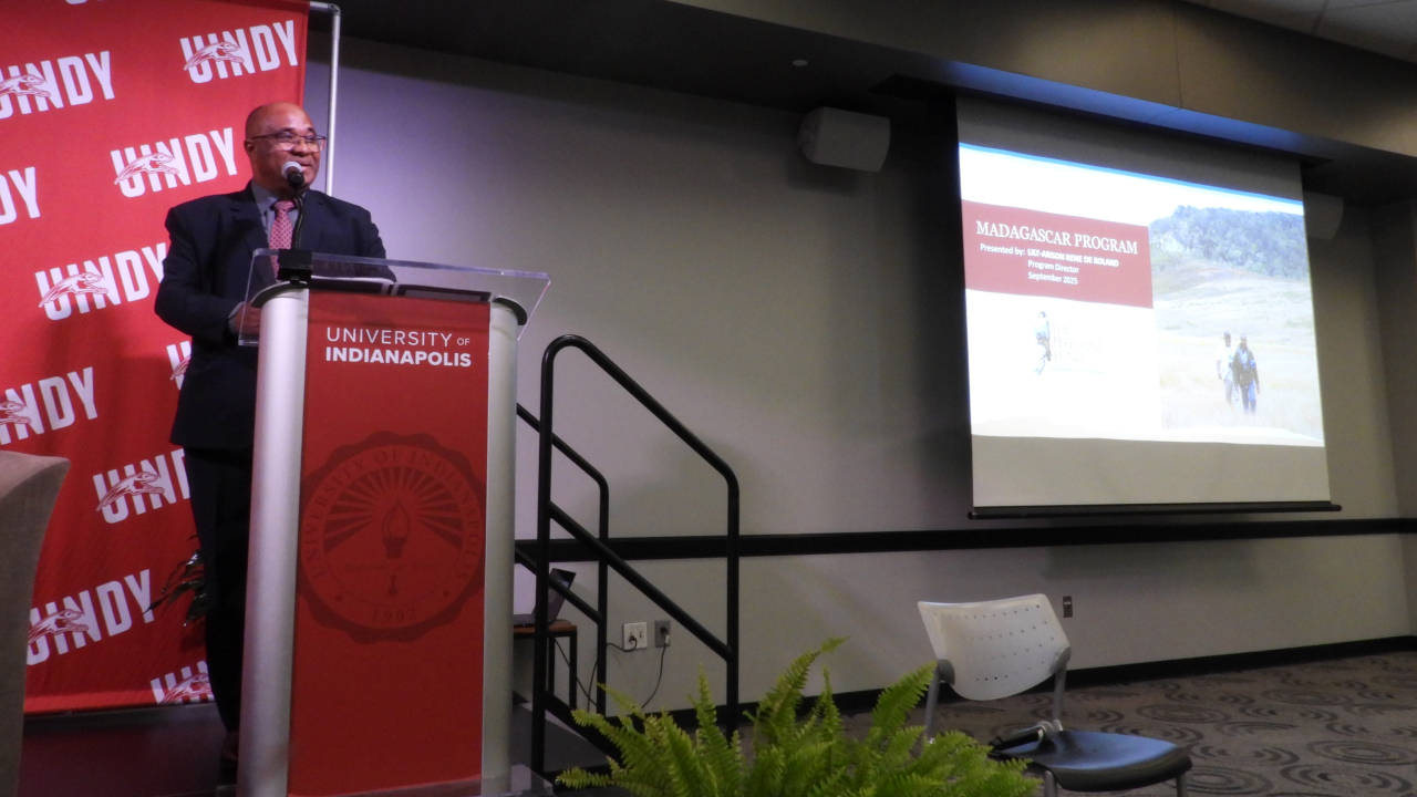 Lily at a podium next to a screen during a talk at the University of Indianapolis