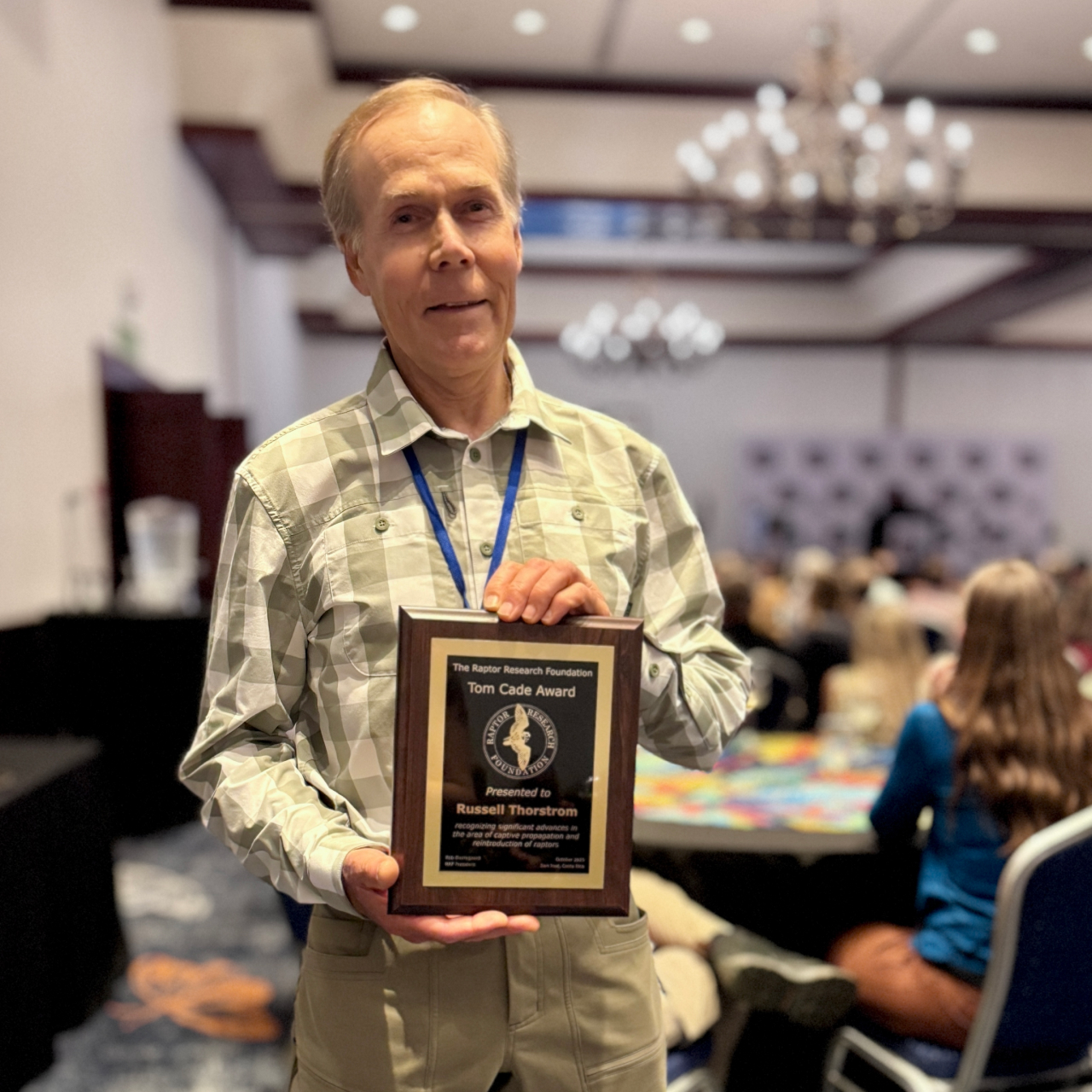 Russell Thorstrom posing while holding the 2025 Tom Cade Conservation Award plaque.