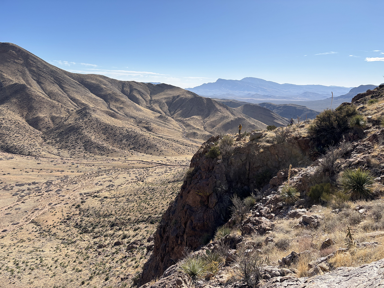 Two biologists looking for Golden Eagles from the top of a cliff overlooking a scenic mountainous landscape in WSMR.