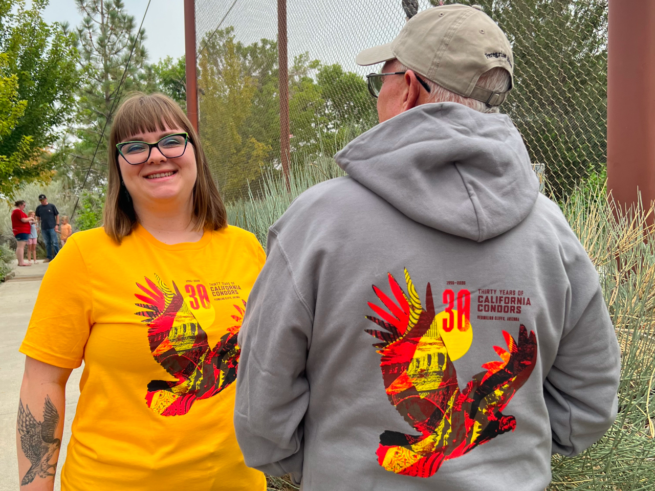 A woman wearing a yellow t-shirt and a man wearing a gray hooded sweatshirt, both featuring the limited-edition design created for the 2026 California Condor release.