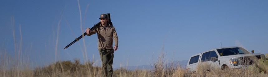 Biologist Tom Hudson carrying a spotting scope and walking away from a truck.