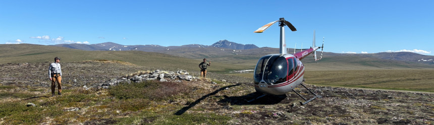 Biologists posing on the open Arctic landscape next to a helicopter with a mountain behind them.