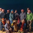 A group of scientists in desert wear at night posing and smiling next to a camel