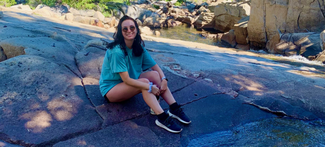 Mackinnon Smith sits on a large rock in the woods