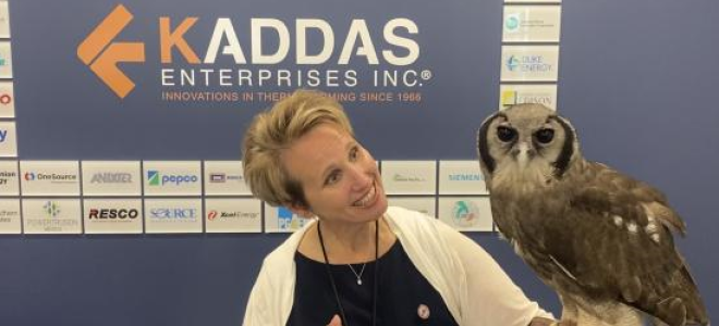 Natalie Kaddas stands in front of the Kaddas Enterprises sign holding Oliver the Verreaux's Eagle-owl on her arm