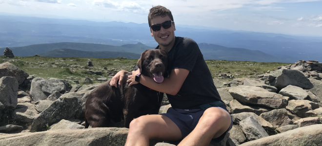 Man holds a dog close while in a field of boulders while on a hike.