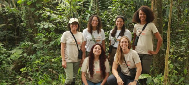 Six biologists in matching t-shirts posing for a group photo in dense forest