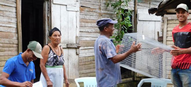 A biologist handing a chicken coop to a member of the public while another resident and another biologist look on