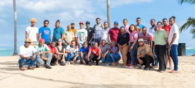 A large team of biologists posing together on a beach with palm trees behind them