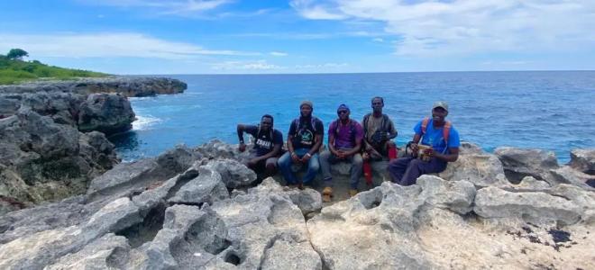 Four biologists seated on a rocky cliff with the ocean visible behind them