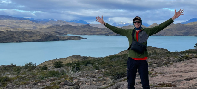 Burr Tweedy standing with his arms raised in front of a lake and distant snow-capped mountains.