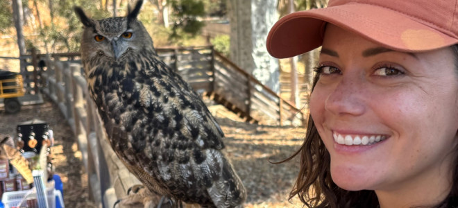 Maggie Holsten posing and smiling next to a perched ambassador Eurasian Eagle-owl.