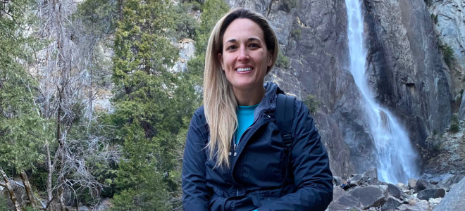 Teresa Cuevas sitting on a log in front of a small waterfall.