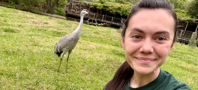 A selfie of Nichole Moore with a banded Sandhill Crane behind her.