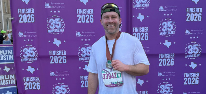 Chris Strojan posing in front of a banner for finishers of the 2026 Austin Marathon.