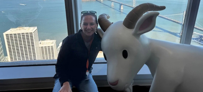 Stacie Johnson posing next to a statue of a goat in front of a high window with lower buildings and a waterfront in the background