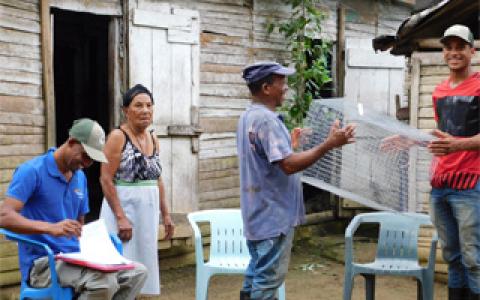 A biologist handing a chicken coop to a member of the public while another resident and another biologist look on