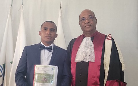 A student carrying a binder posing next to a professor in graduation robes.