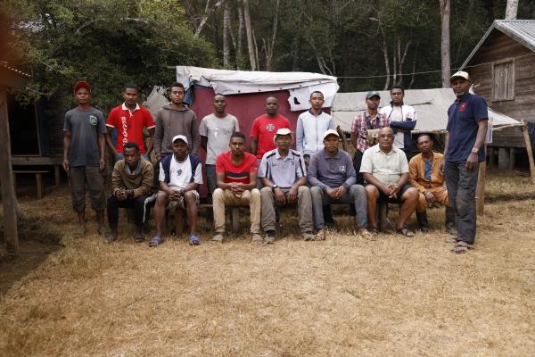 Sixteen men, all part of the field team, posing for a photo at camp