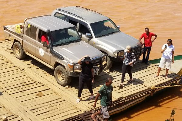 People and vehicles on a wooden ferry bringing them across the Tsirbihina River