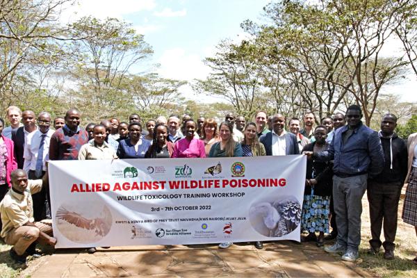 A group of 42 people gathered around a sign with the words &quot;Allied Against Wildlife Poisoning&quot;