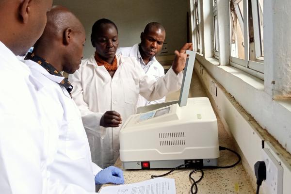 Four people in lab coats gathered around a lab testing device