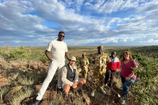 Six people, two of which are wearing military uniforms, pose for a photo near conservation based vulture feeding area