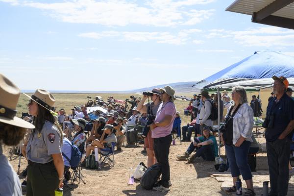 A group of people with spotting scopes and binoculars looking off to the left of screen