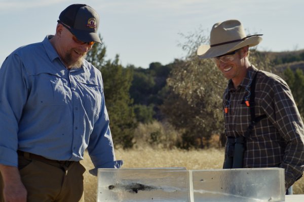 Two hunters smiling and examining a block of clear gel with bullet fragments in it