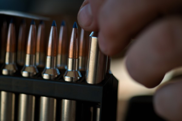 A closeup of a hand placing a copper bullet into a rack of others