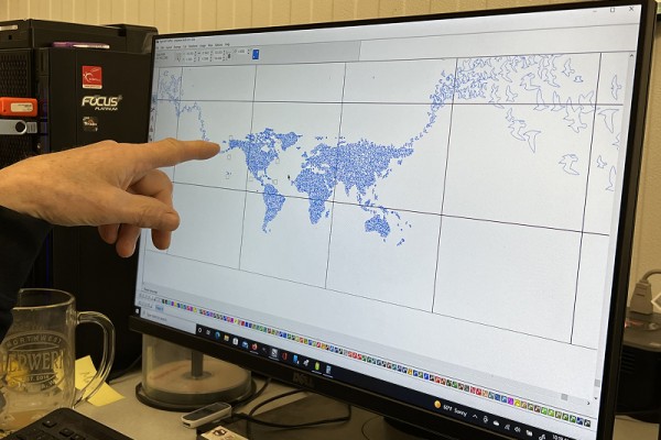 A hand points to a computer screen featuring a revised design. The circular murmuration has been straightened from the original, along with other smaller alterations.