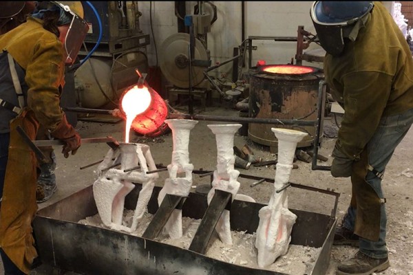 Two people in protective gear pouring molten metal into molds.