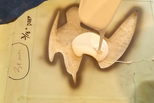 Epoxy being poured into a shorebird silhouette sand-blasted into a rock sample.