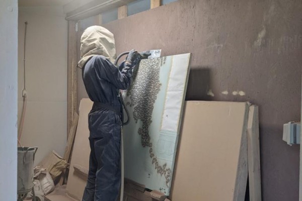 An artist in protective gear sandblasting a stone tile.