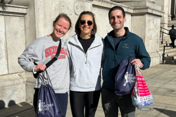 TPF 2025 TCS NYC Marathon team members Tali Brennan, Karleigh Page, and William Gingold pose for a photo holding swag bags containing their team gear before the race.