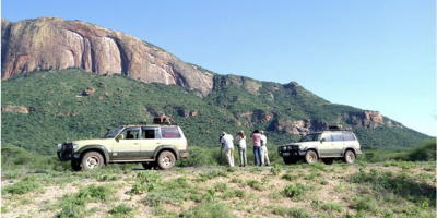Biologists beside SUVS below cliff face, monitoring raptors