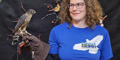 A woman holds a falcon on a falconry glove on her hand.