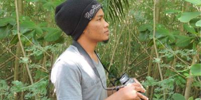 A biologist in dense vegetation holding up a pair of binoculars