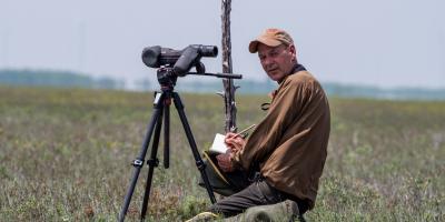 Brian Mutch behind scope with notebook, looking at camera