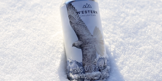 Beer can in the snow with a watercolor scene on the label of a Gyrfalcon flying with a mountainous, snowy landscape in the background