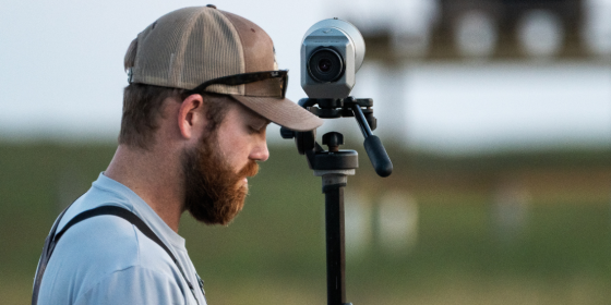 Biologist Tom Hudson behind a scope with Aplomado Falcon nest in background