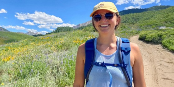 Karleigh Page standing on a dirt trail with a scenic view of wildflowers and rolling hills behind her.