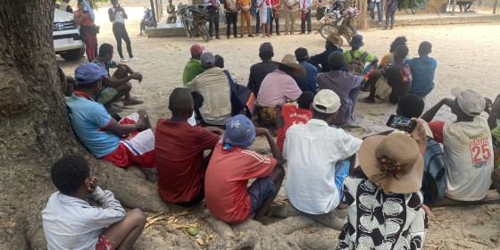 A collection of community members seated on the ground listening to community leaders speaking with Peregrine Fund staff members.