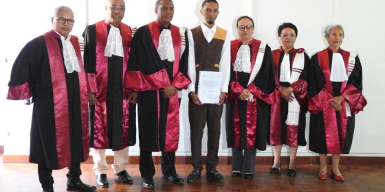 A student holding a diploma posing with six people in academic dress.