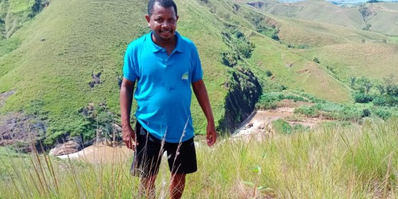 Michel Rakotoson walking up a grassy trail with grass-covered distant hills behind him.