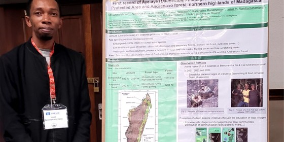 A Madagascar team member at a conference posing alongside a research poster he is presenting.