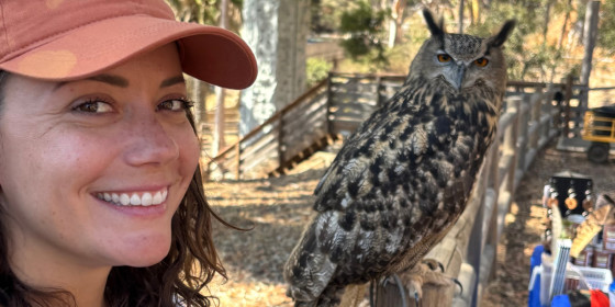 Maggie Holsten posing and smiling next to a perched ambassador Eurasian Eagle-owl.