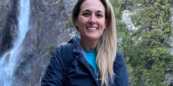 Teresa Cuevas sitting on a log in front of a small waterfall.